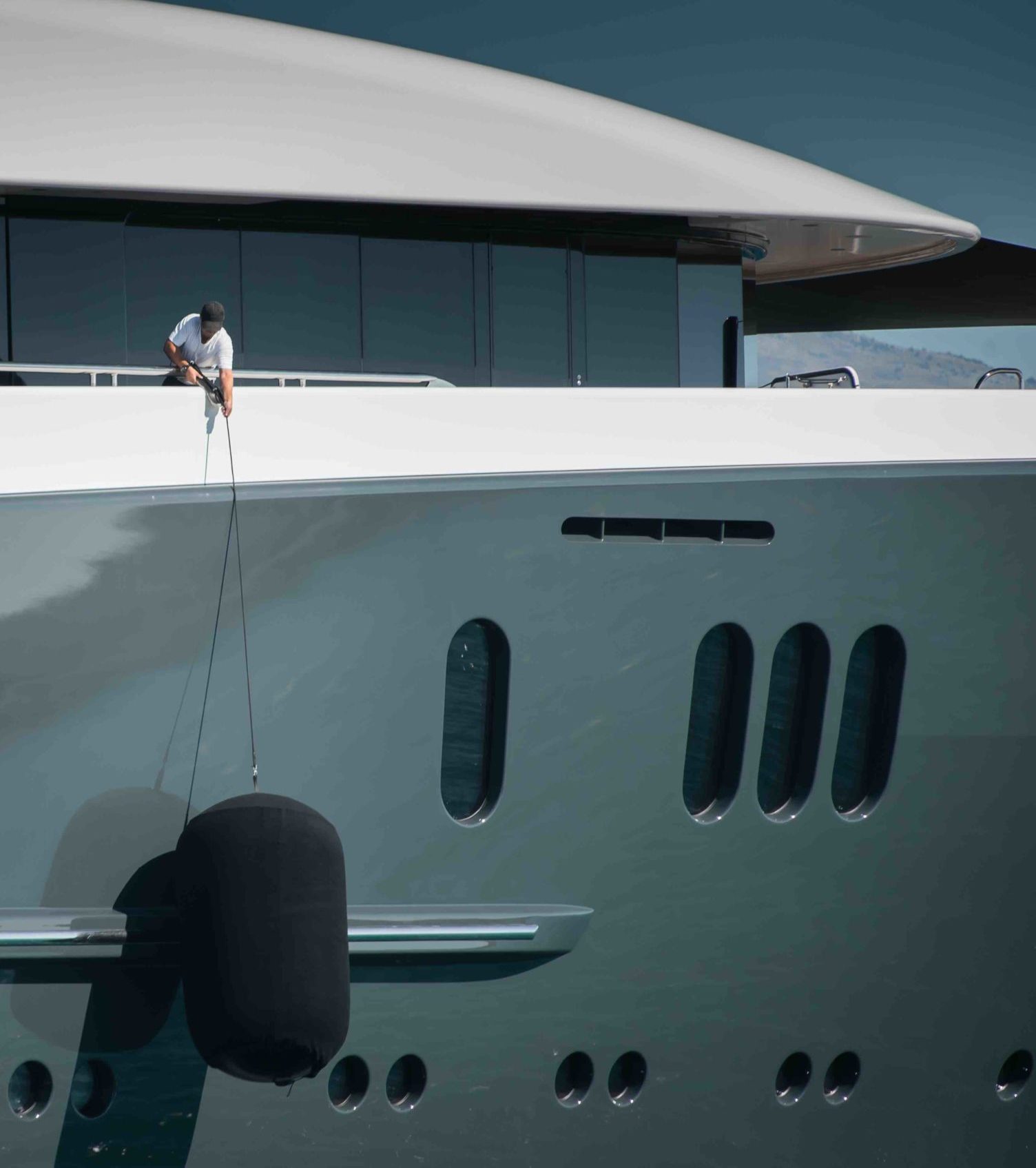 Detail of beautiful Superyacht, deckhand lifting the huge fender of the starboard side of the megayacht, spotless grey and white superstructure