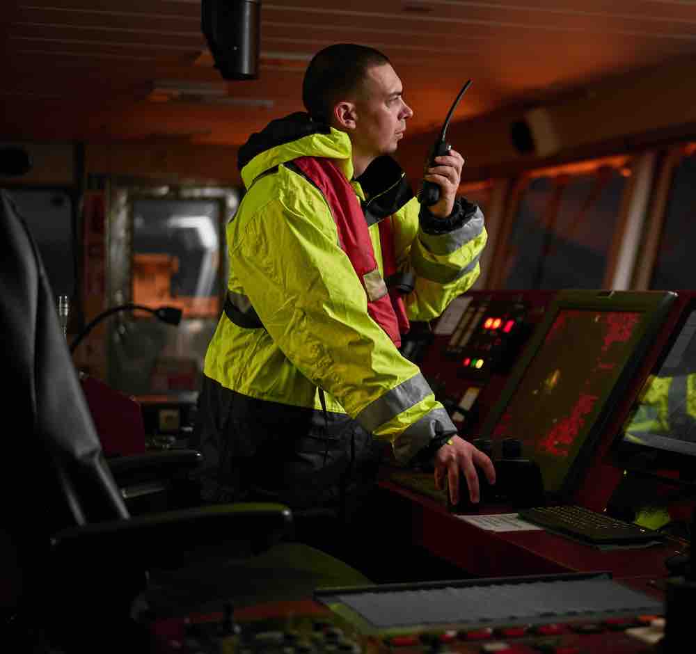 Navigator, pilot, captain part of ship crew performing daily duties with VHF radio, binoculars, logbook, standing nearby to ECDIS and radar station on board of modern ship with high quality equipment