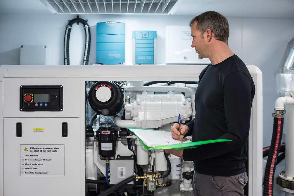 Caucasian Male Superyacht Engineer working on the engine room, inspecting the generator with checklist folder and pen in his hand