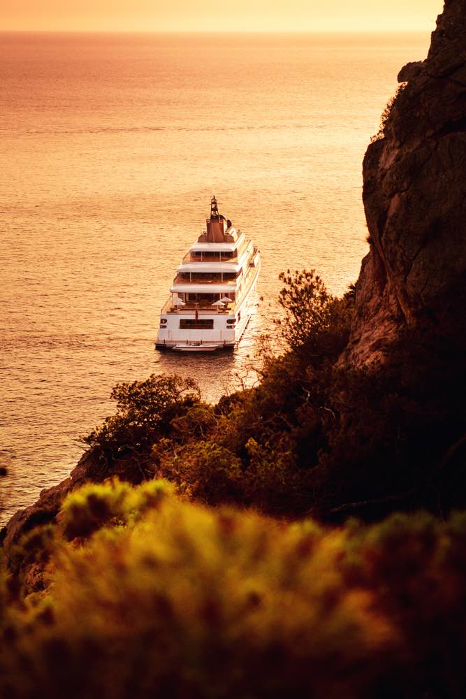 Beautiful private luxury superyacht anchored of the coastline of the spanish island in golden sunset colorful glow. View down to the sea from the nature landscape. Port d' Andratx, Mallorca