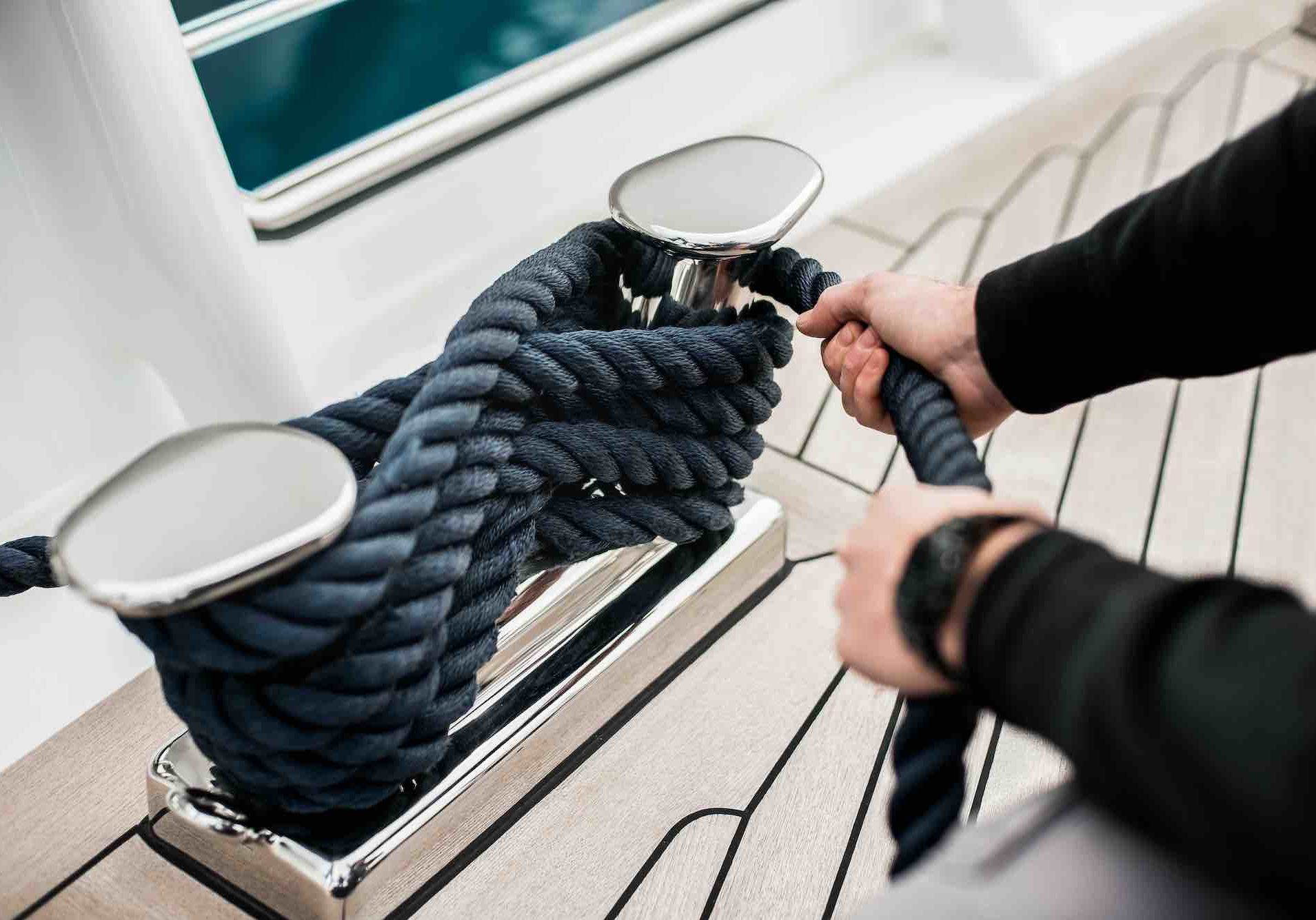 Detail of hands cleating off superyacht mooring lines on the foredeck with teak deck and stainless steel fittings
