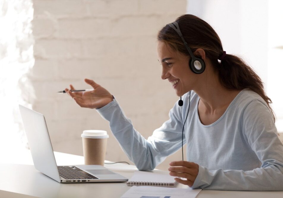 Side view head shot smiling mixed race lady freelancer wearing headset, communicating with client via video computer call. Millennial pleasant professional female tutor giving online language class.